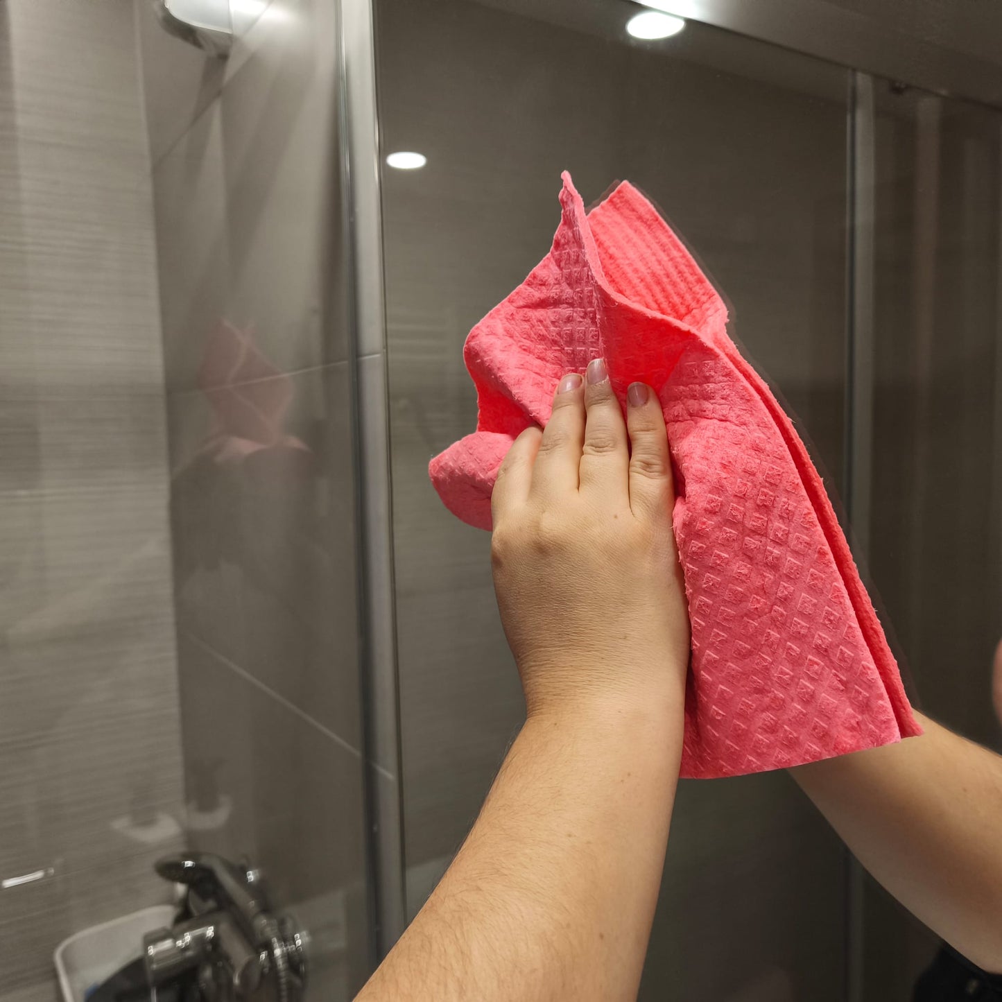Mano usando una bayeta reutilizable rosa para limpiar el cristal de la ducha