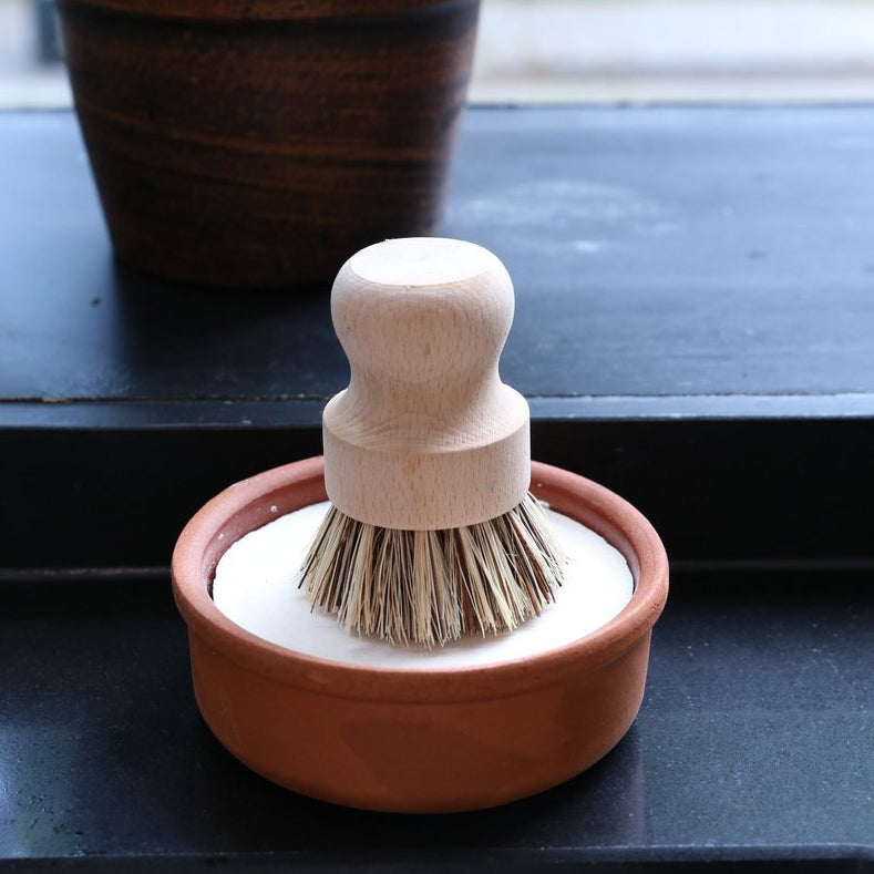 jabon natural para vajilla en recipiente de cerámica y con cepillo de mango corto para fregar los platos