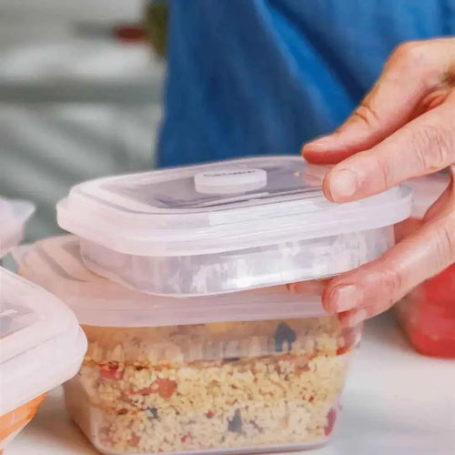 Manos sosteniendo un tupper plegable de silicona transparente con comida, recipiente reutilizable y ecológico